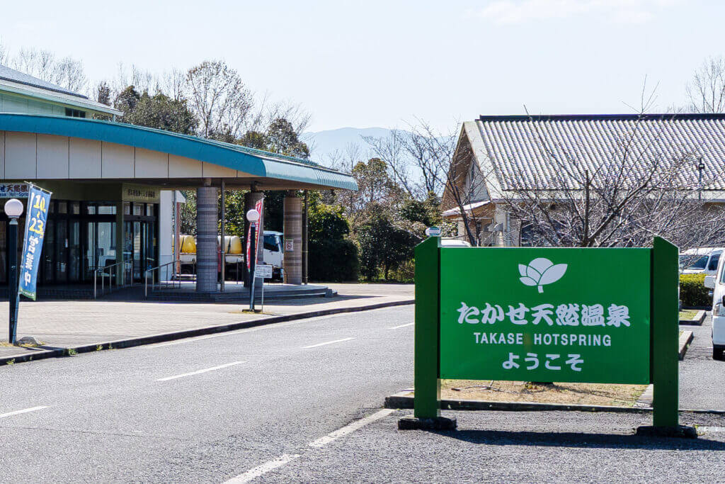 『たかせ天然温泉 ようこそ』と書かれた緑色の看板と、施設の入り口外観